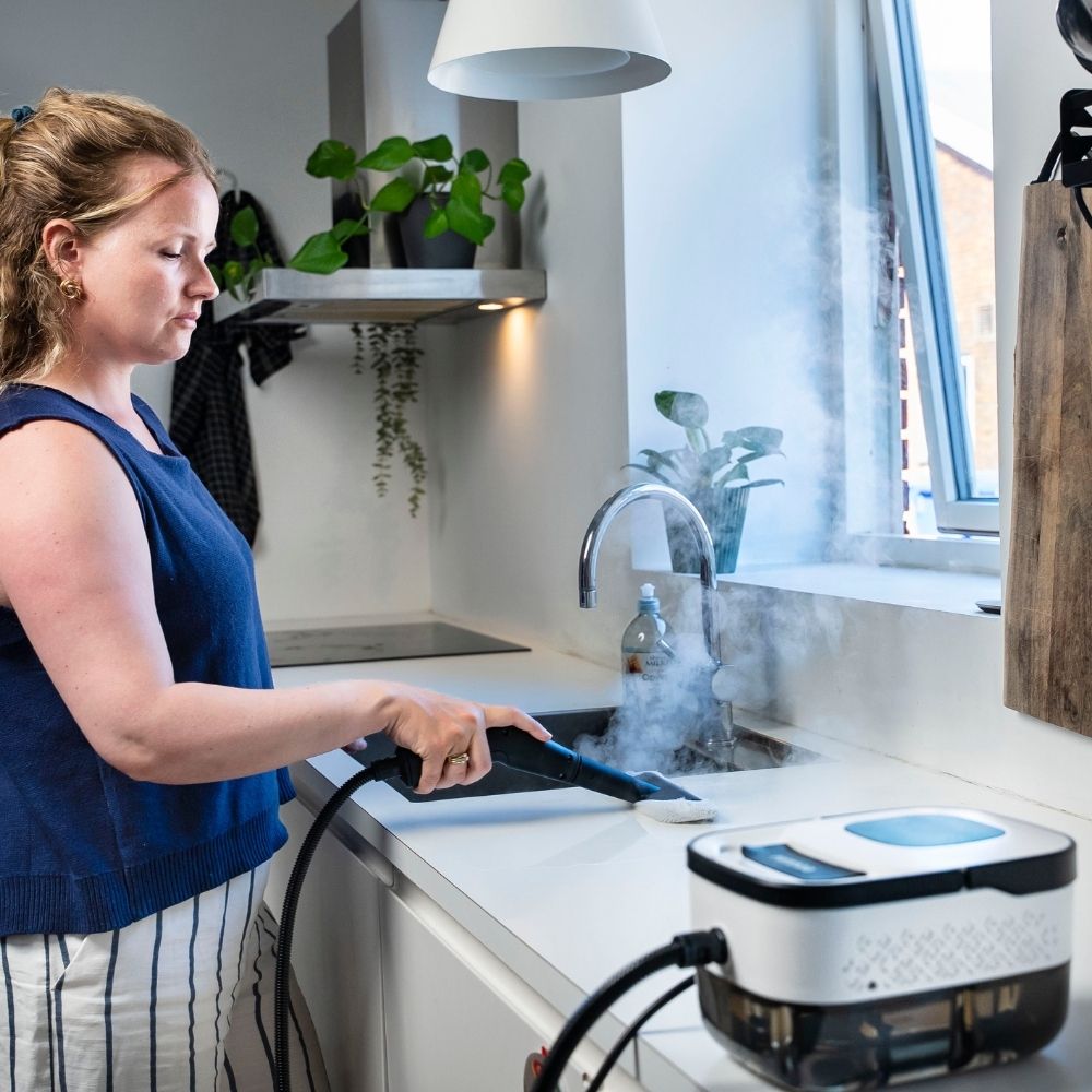 Person bruger damprenser til at rengøre køkkenvask og bordplade